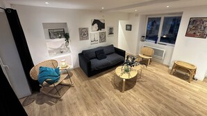 A modern living room with a grey sofa, a round coffee table, and a wicker chair. - Charming house with garden near Lyon, airport and Eurexpo (Jonage)