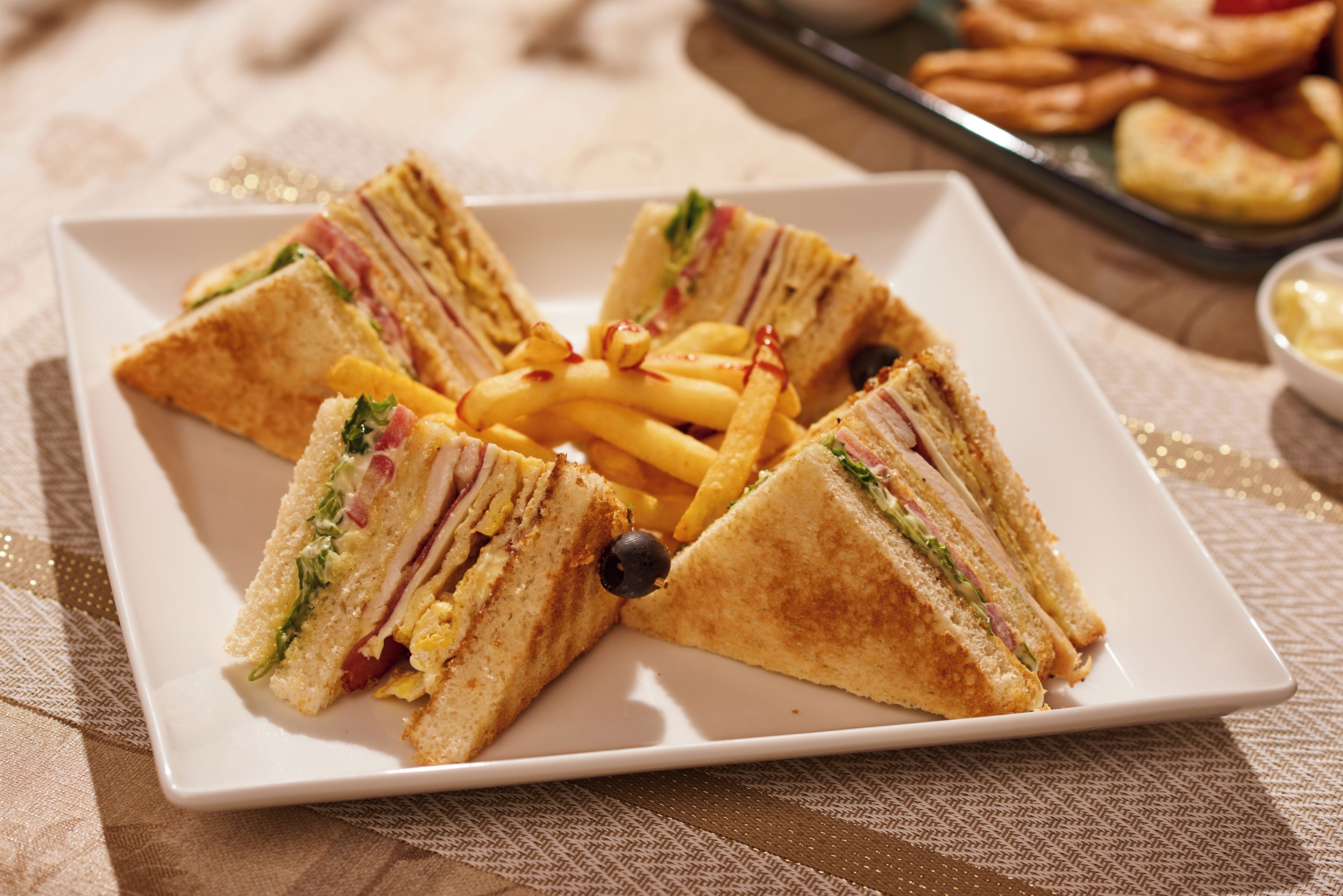 Un plato de sándwiches triangulares con papas fritas, servido sobre un plato blanco cuadrado.