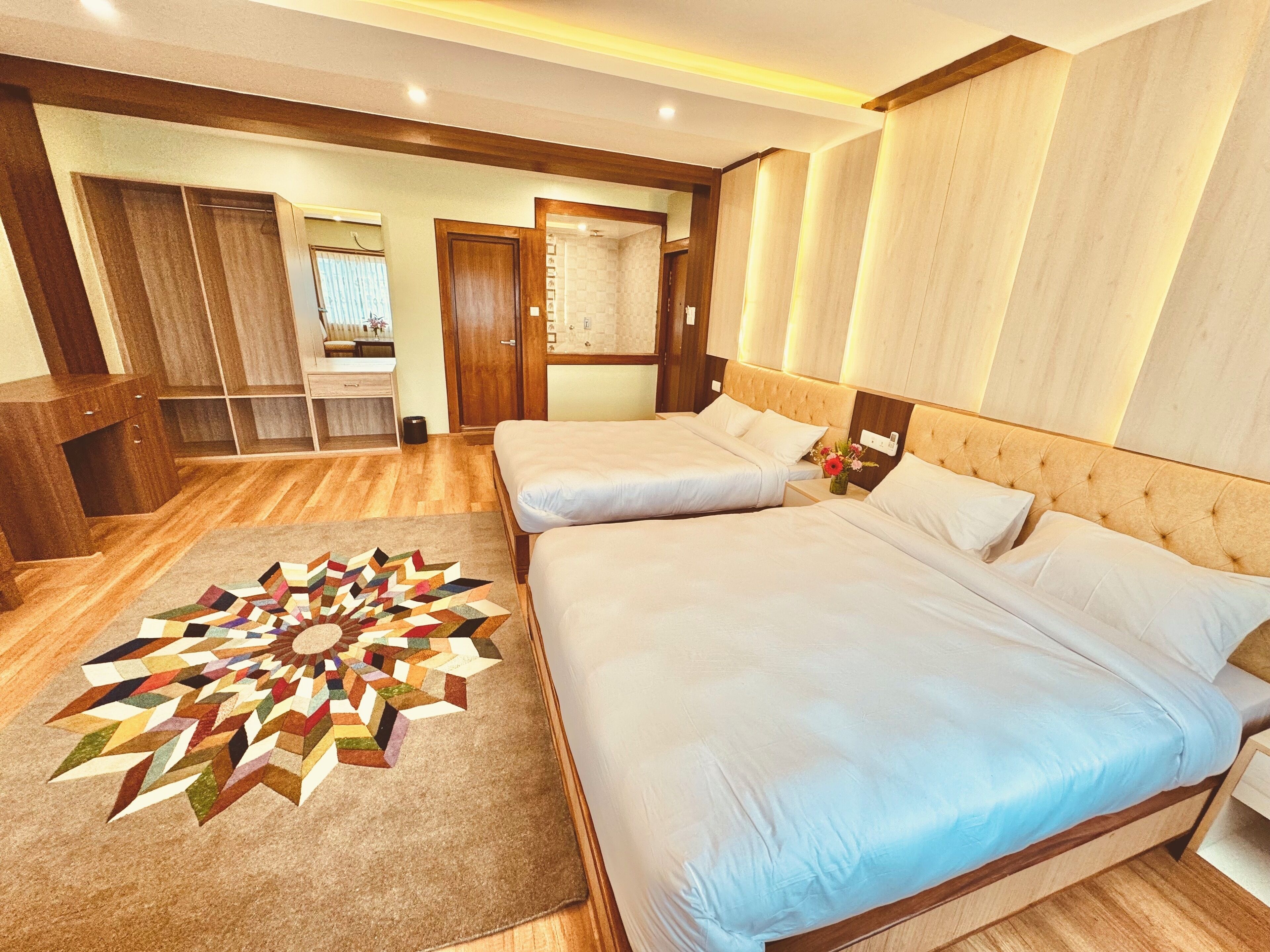 Habitación de hotel con dos camas, suelo de madera, alfombra geométrica y armario de madera.