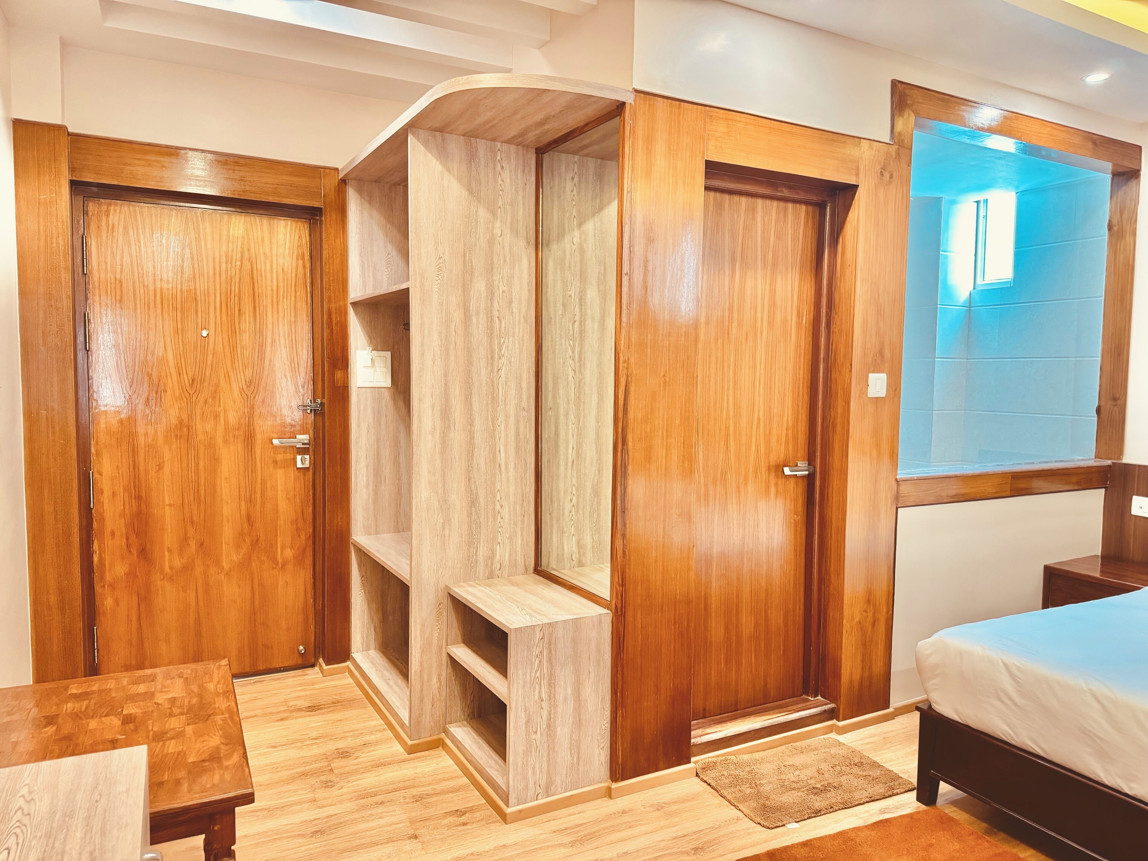 A bedroom with wooden wardrobes, a bed, a small table, and a built-in shelving unit.