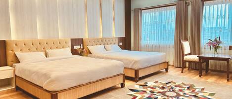 A hotel room with two beds, a wooden floor, a patterned rug, and a desk with a chair.