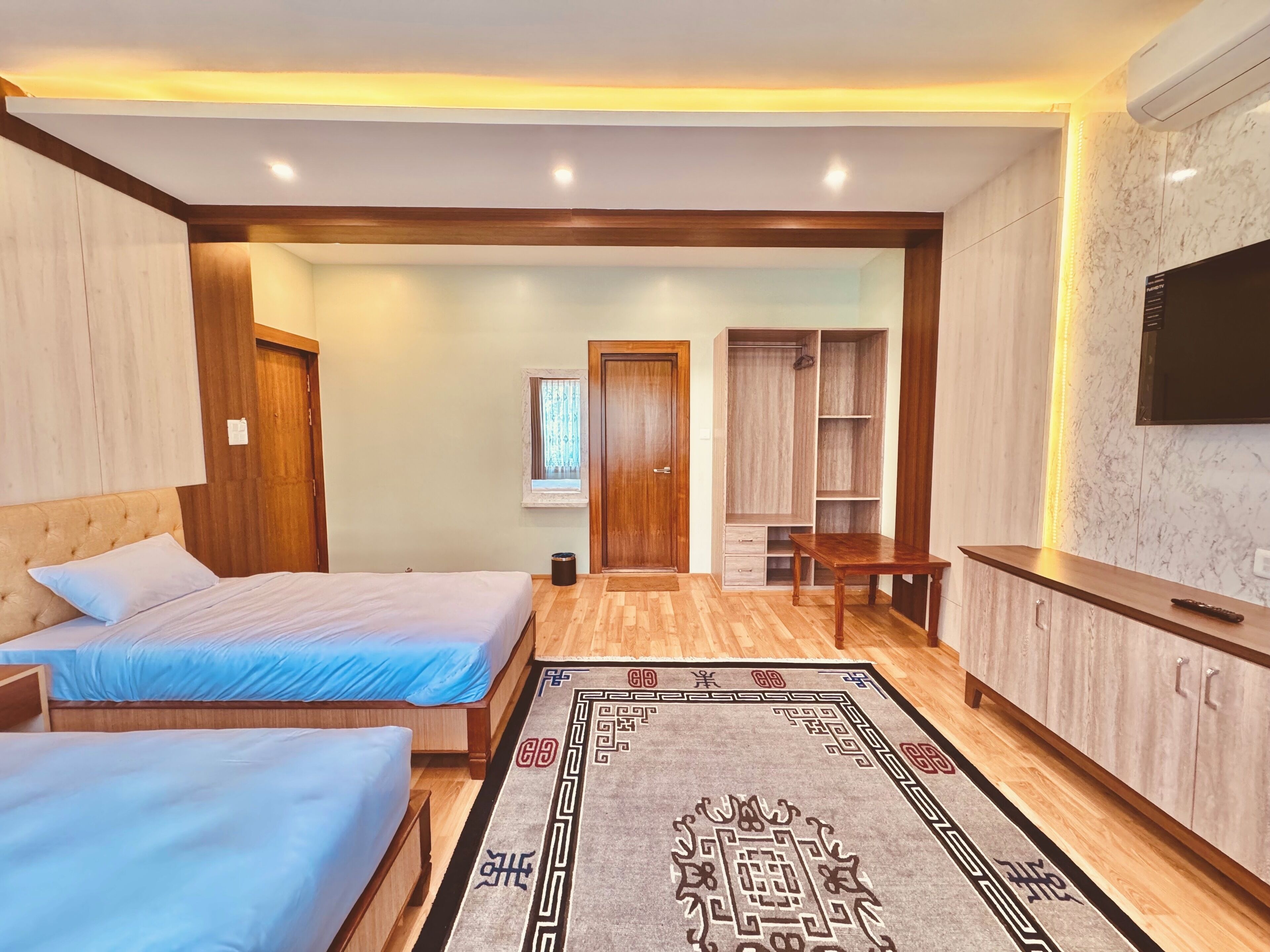 A bedroom with two beds, a wardrobe, a TV, and a small table.