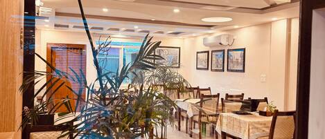 A modern dining area with tables and chairs, surrounded by potted plants and framed pictures on the walls.