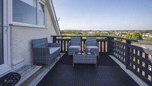 Un balcón con muebles de mimbre, vista a un pueblo y cielo despejado.