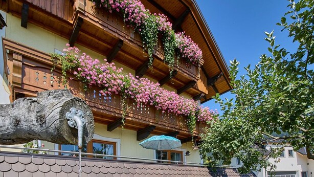 A traditional wooden building with flower boxes on the balcony and a small water feature in front. - Krapflhof (Weisspriach)