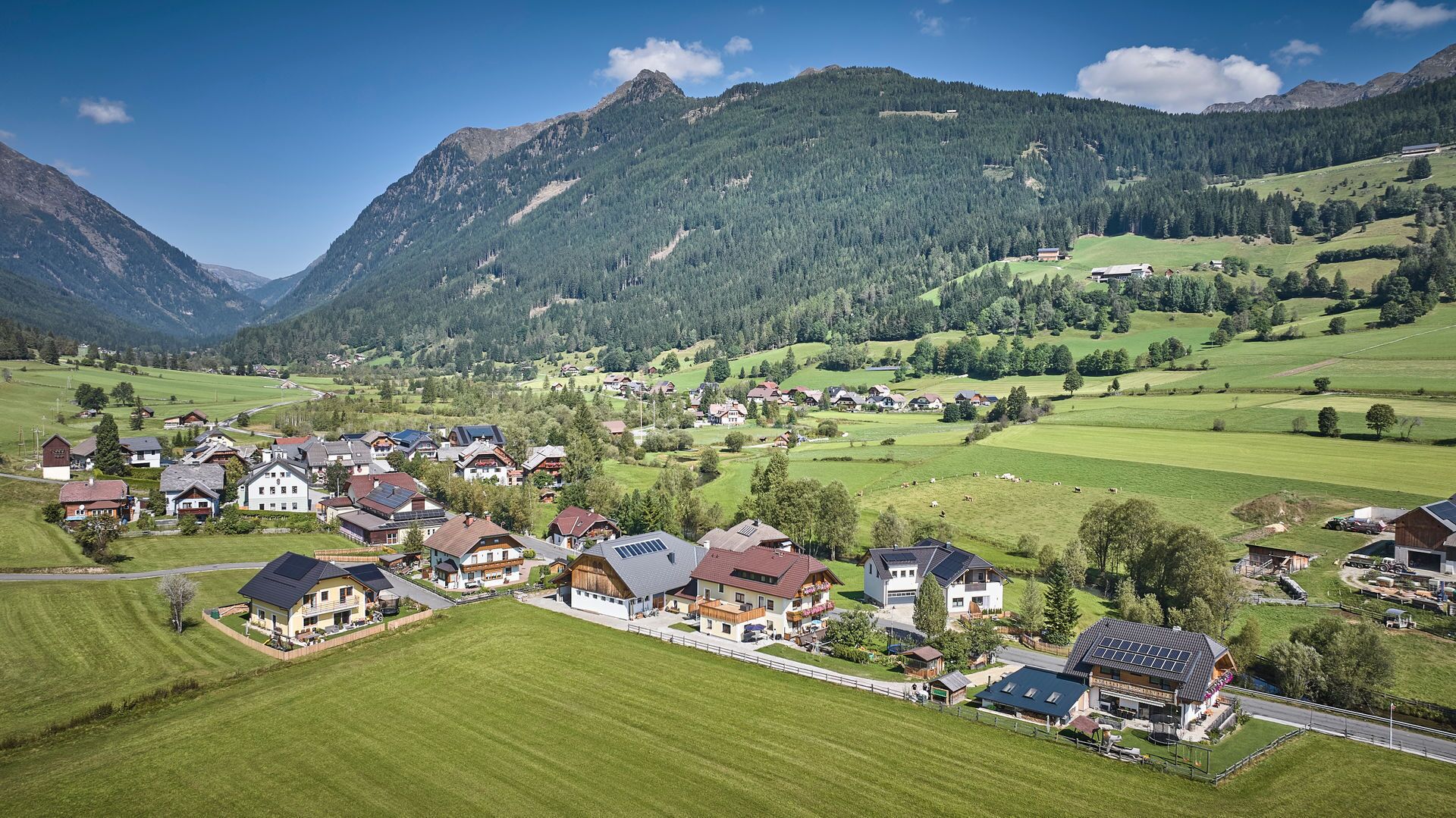 Ein ländliches Dorf mit Häusern, grünen Feldern und Bergen im Hintergrund.