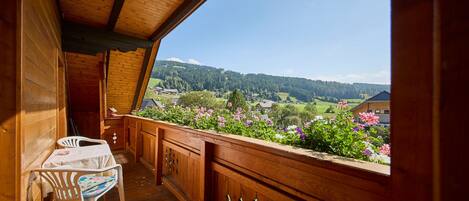 Ein hölzerner Balkon mit Tisch und Stühlen, der auf eine malerische Landschaft mit Häusern und Grünblicken blickt.