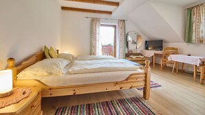A bedroom with a wooden bed, a desk with a chair, a television, and a window with curtains. - Krapflhof (Weisspriach)