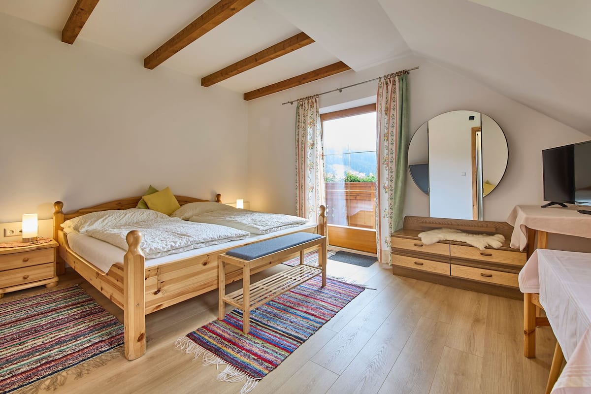 A bedroom with a wooden bed, bedside tables, a bench, a dresser, a mirror, and a television.