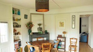 A dining area with a wooden table and chairs, surrounded by shelves with books and decorative items. - Apt with garden and parking on the banks of the Seine in front of the cathedral (Rouen)