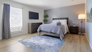 A bedroom with a bed, a nightstand, a lamp, a TV, and a window with curtains. - Hoff Gardens 39 - 2BR 2BA - Downtown Lubbock (Lubbock)