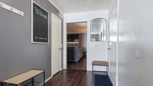 A hallway with a bench, a welcome sign, a door leading to a kitchen, and a mirror on the wall. - Hoff Gardens 39 - 2BR 2BA - Downtown Lubbock (Lubbock)