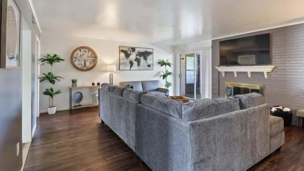 A living room with a grey sectional sofa, a round wooden table, and two potted plants. - Hoff Gardens 39 - 2BR 2BA - Downtown Lubbock (Lubbock)