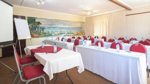 A conference room with white tables, red chairs, and a painting of a beach scene on the wall. - Oak Lodge Guesthouse (Makhanda)