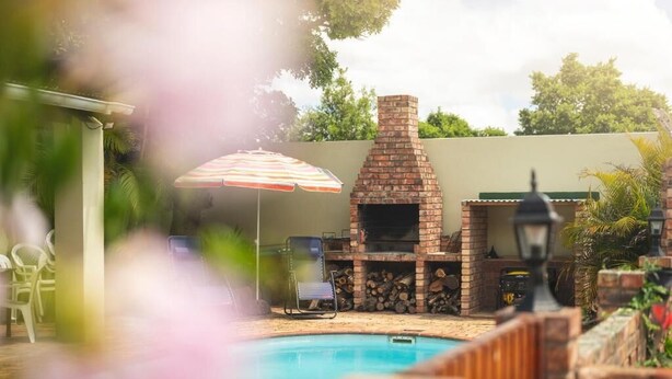 A backyard with a brick fireplace, a pool, and outdoor furniture. - Oak Lodge Guesthouse (Makhanda)