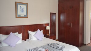 A hotel room with a large bed, wooden wardrobe, a framed picture on the wall, and a bedside table with a lamp. - Oak Lodge Guesthouse (Makhanda)