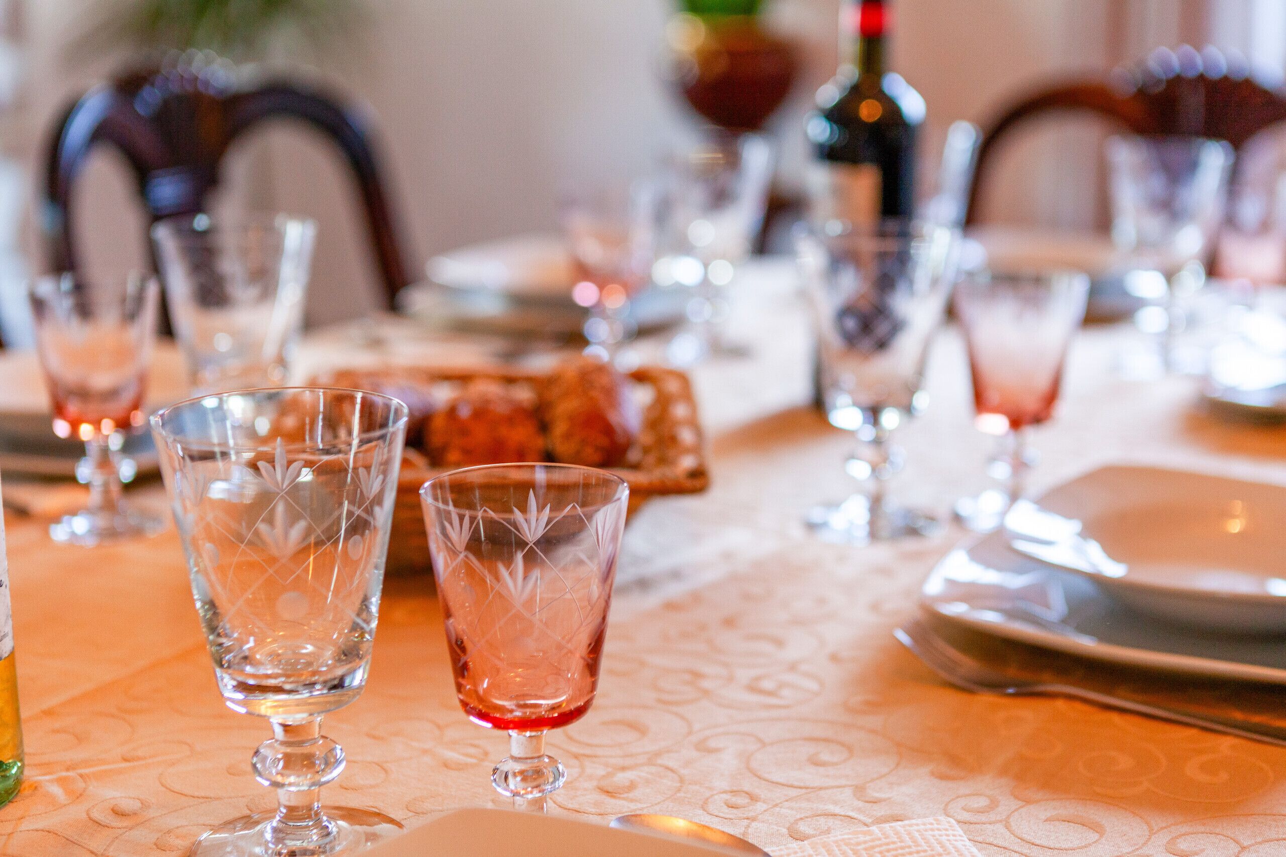 A dining table set with clear glassware and plates, a bottle of red wine, and a small dish of food.
