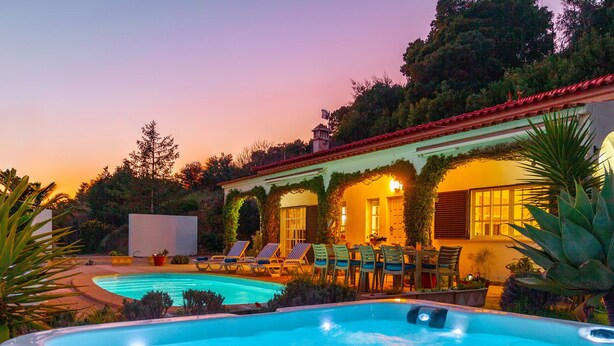 A swimming pool with lounge chairs and a dining area, surrounded by greenery and a building with a red roof. - Villa Monchique Royal (Monchique)