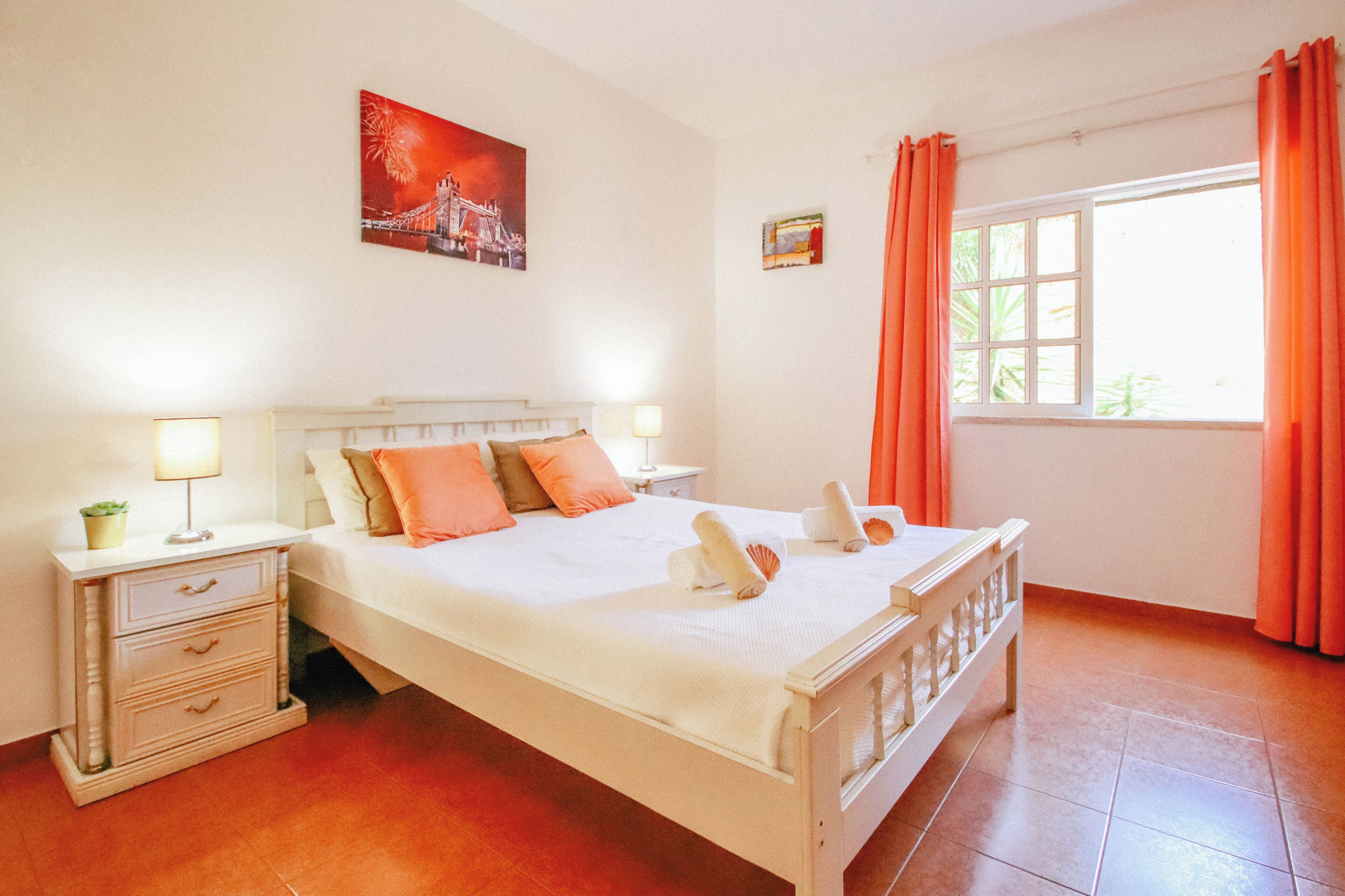 Quarto bem arrumado com cama, mesas de cabeceira e janela com cortinas.