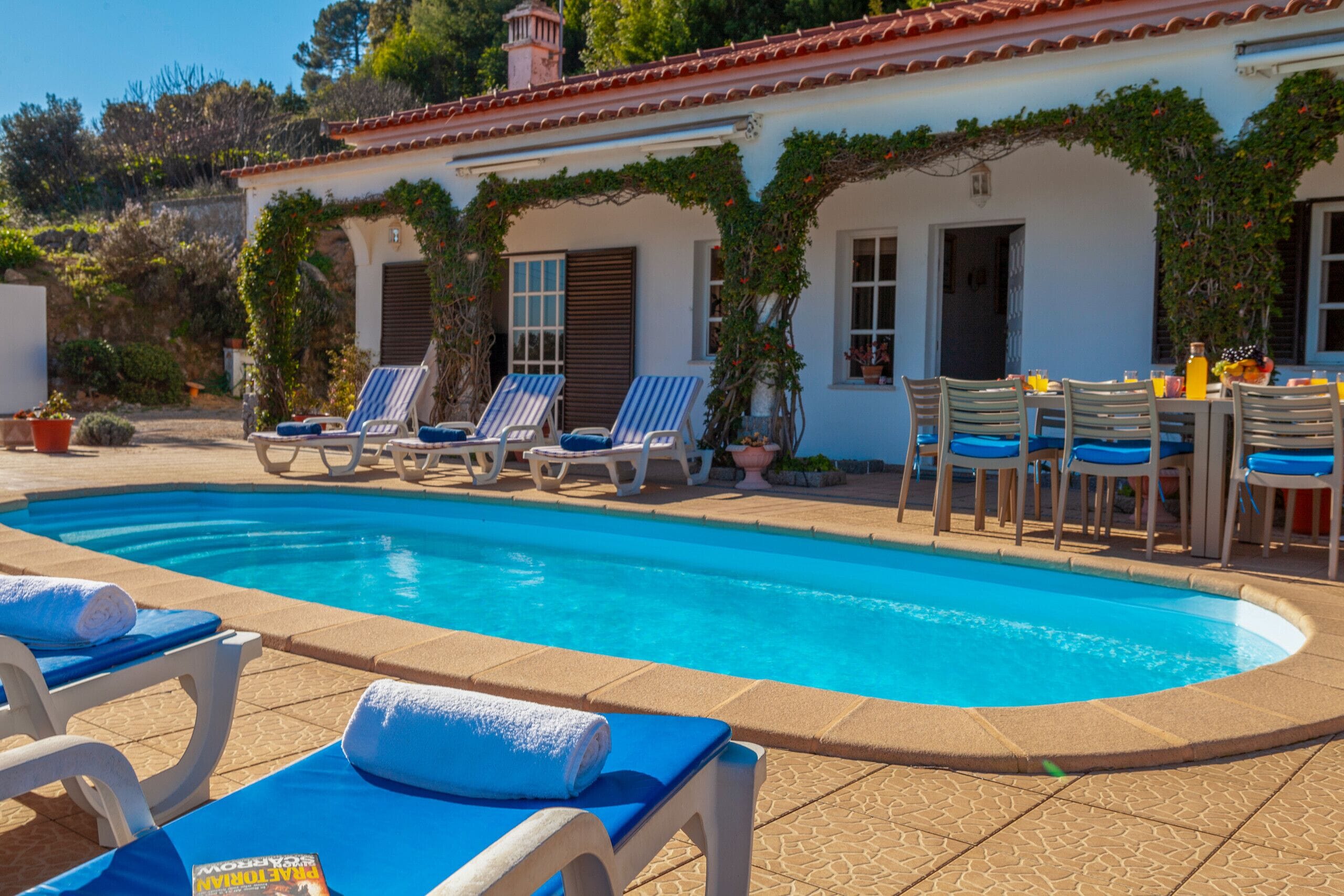 Zona de piscina con sillones reclinables y mesa dispuesta para comer.