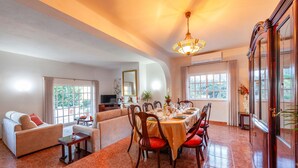A spacious living area with a dining table set for six, surrounded by wooden chairs with red cushions. There is a sofa and a small table with a bottle on it. - Villa Monchique Royal (Monchique)