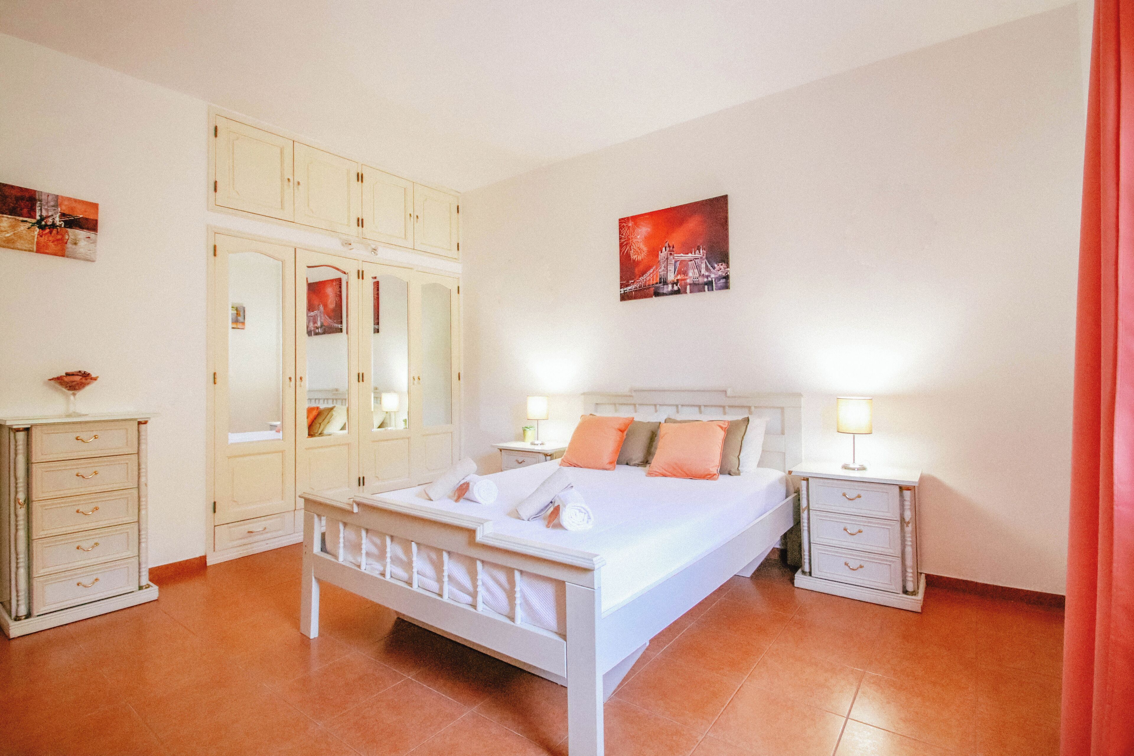 Un dormitorio ordenado con cama, mesitas de noche, armario y espejo.