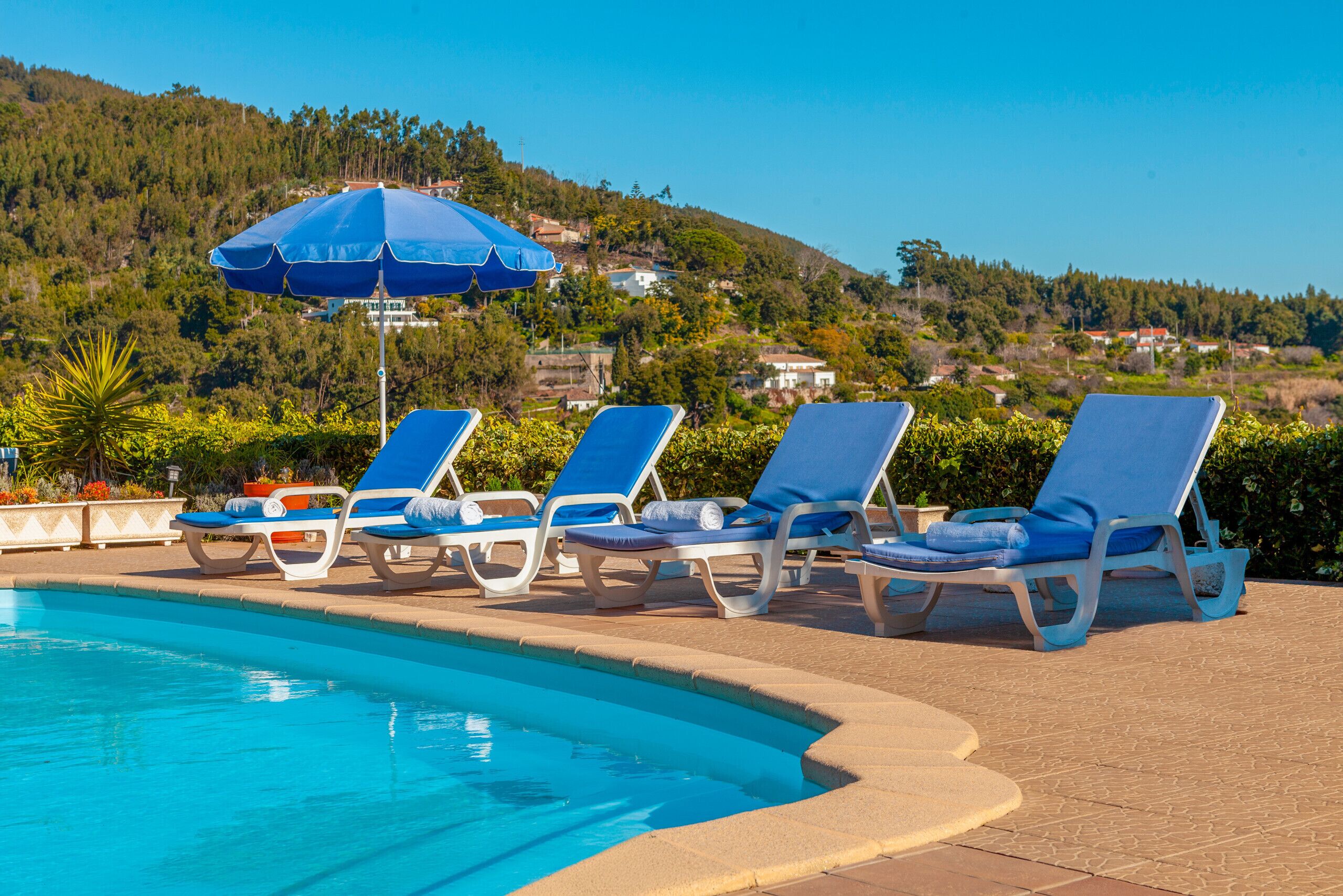 Área de piscina com espreguiçadeiras e um guarda-sol azul.