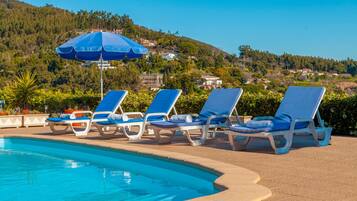 Área de piscina com espreguiçadeiras e um guarda-sol azul.