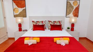 Quarto de hotel com uma cama grande, roupa de cama vermelha e branca, duas luminárias vermelhas e duas pinturas abstratas nas paredes.