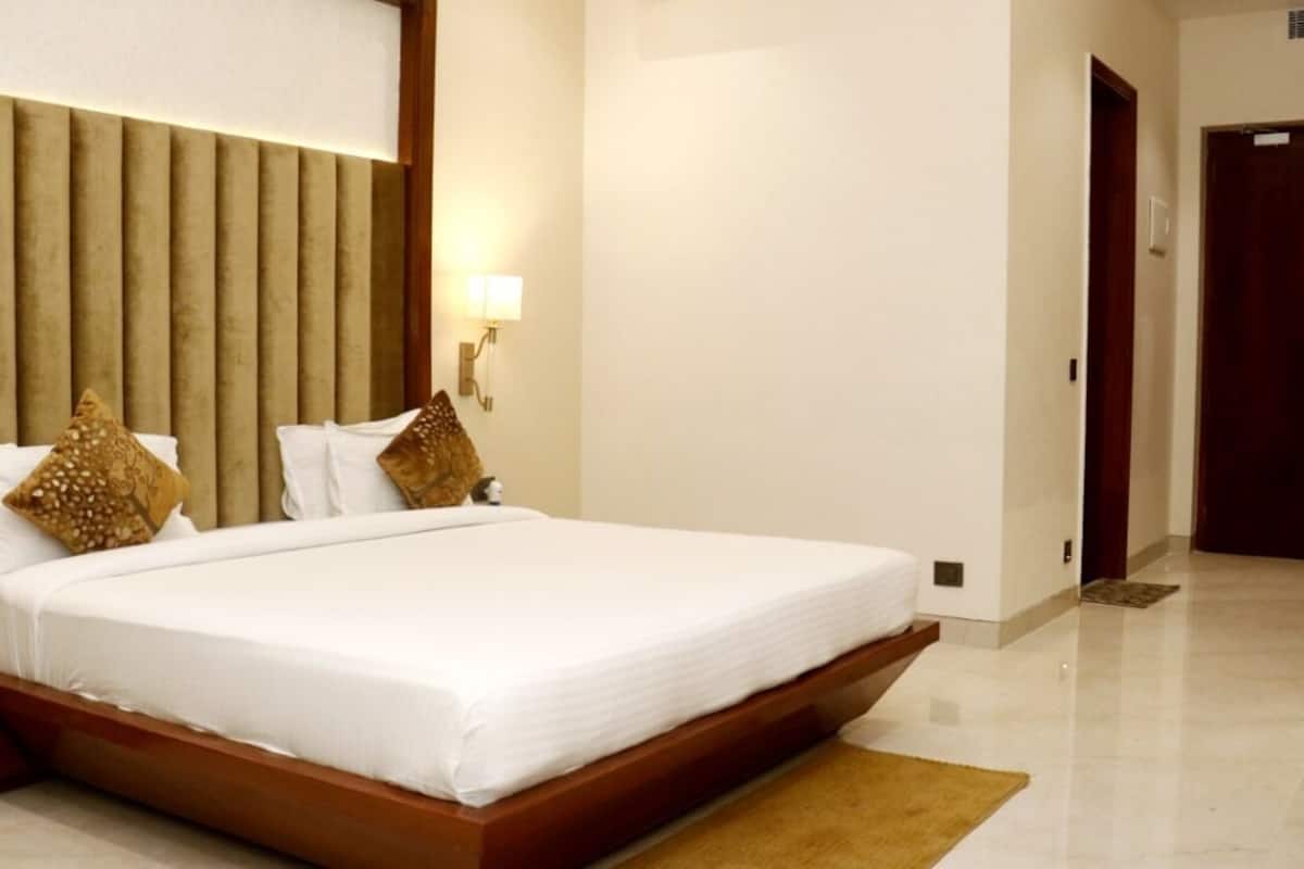 A hotel room with a large bed, a wooden headboard, and a nightstand with a lamp.