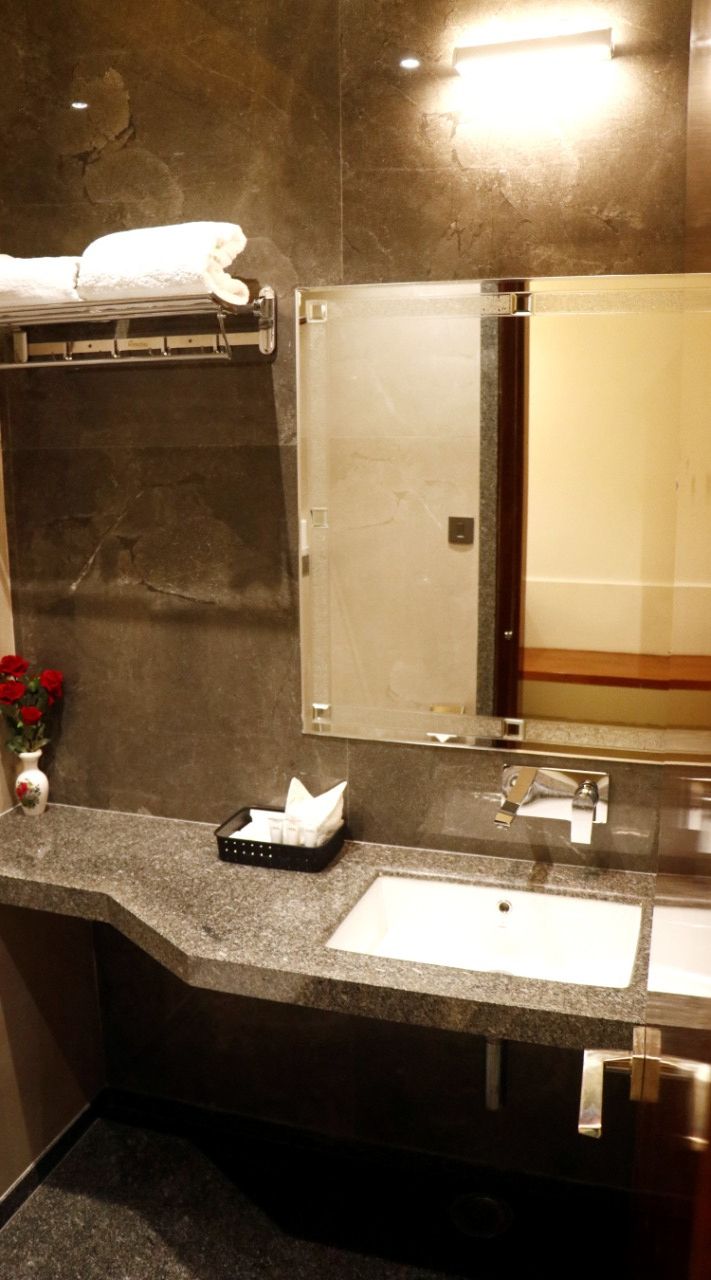 A bathroom with a granite countertop, a white sink, a mirror, and a towel rack.