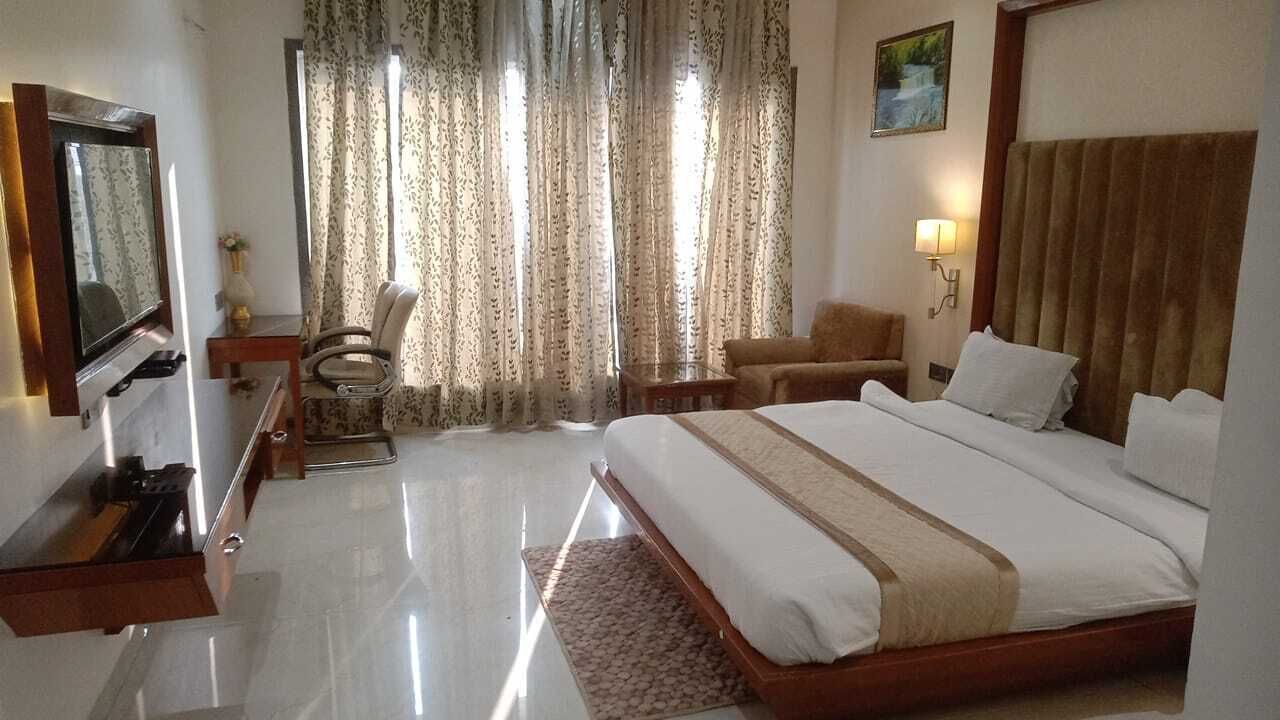 A hotel room with a large bed, a desk, a chair, a TV, and curtains.