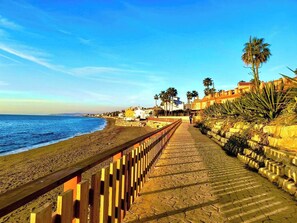 A coastal walkway with a wooden fence, leading to a beach with a clear view of the ocean.