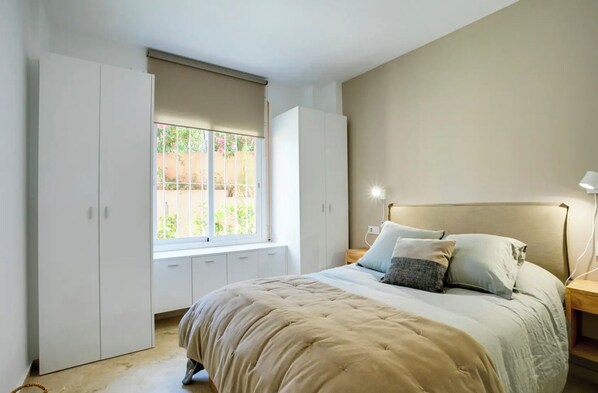 A bedroom with a bed, bedside tables, a window with a view, and built-in wardrobes.