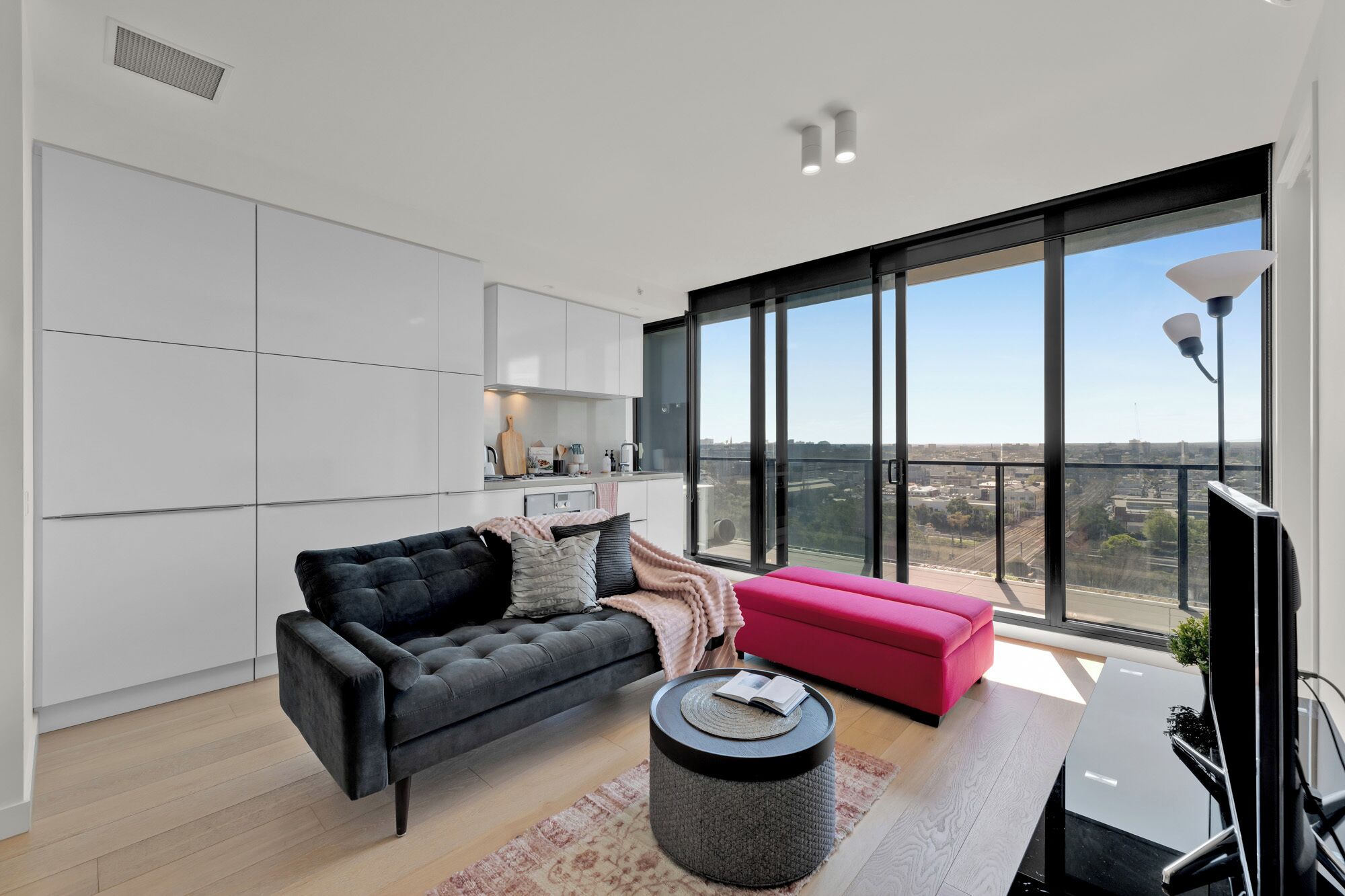 A modern living room with a black sofa, a pink ottoman, and a round coffee table.