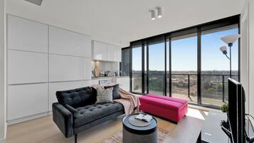 A modern living room with a black sofa, a pink ottoman, and a round coffee table.
