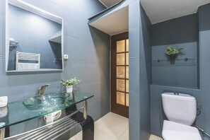 A bathroom with a glass sink, white toilet, and a mirror above the sink.