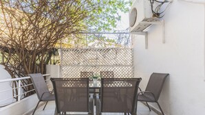An outdoor patio with a table and chairs, a white wall, and a lattice screen.