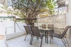 A balcony with a table and chairs, a lattice wall, and a tree.