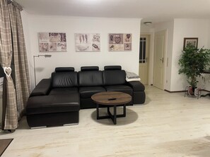 A living room with a black sectional sofa, a round wooden coffee table, and a potted plant.