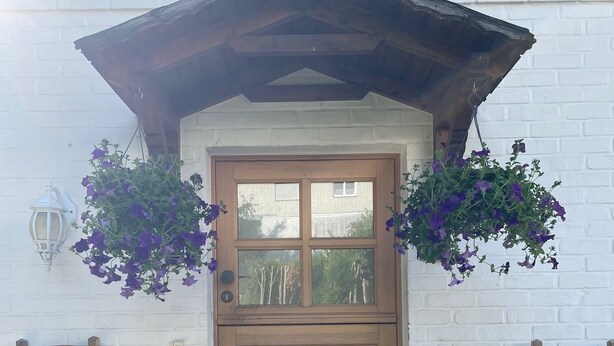 A wooden door with a small window, flanked by two hanging flower baskets. - Newly adapted vacation apartment in the heart of Gemünd (Schleiden)