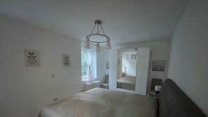 A bedroom with a bed, a mirror, a window with curtains, and wall art. - Newly adapted vacation apartment in the heart of Gemünd (Schleiden)