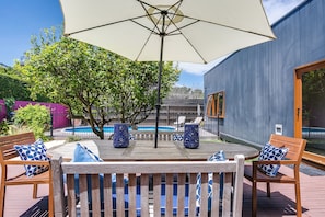 Relax by the poolside with a shaded patio area, complete with a table and chairs.