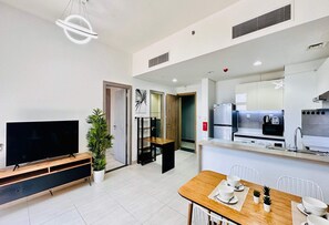 A modern kitchen with a refrigerator, microwave, and stove. There is a dining area with a table and chairs. A television is on a wooden stand.