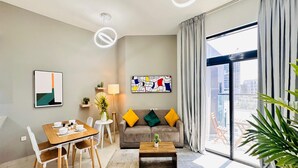 A modern living room with a dining area, a sofa with colorful cushions, a coffee table, and a large window with a view of buildings.