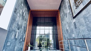 A modern building entrance with a glass door, a wooden slatted wall, and a metal staircase.