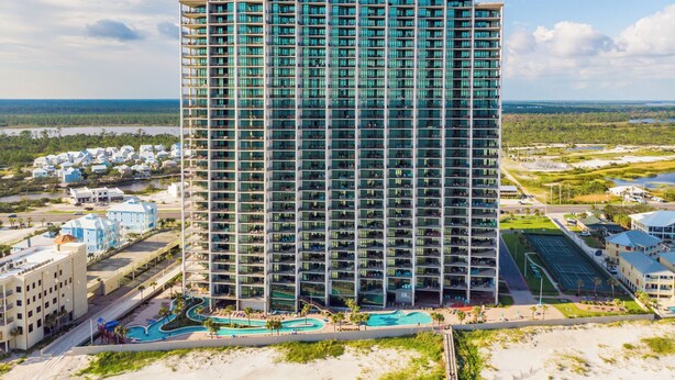 A high-rise hotel with multiple balconies, a swimming pool, and a view of the surrounding landscape.