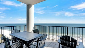 A balcony with a table and chairs, overlooking a beach with a clear view of the ocean.