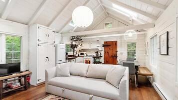 A cozy living room with a sofa, a TV on a wooden stand, and a kitchen in the background.