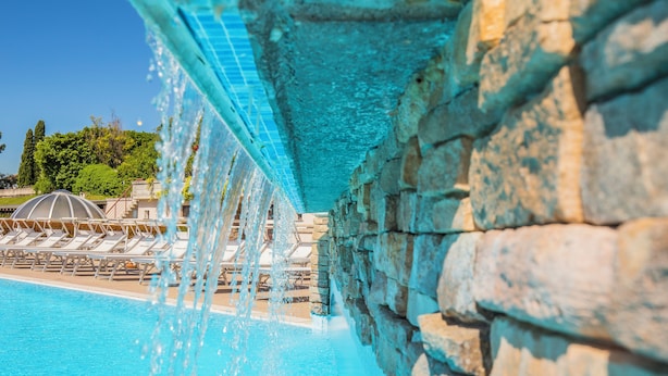A swimming pool with a stone wall and a water feature. - Marina Loft (Moniga del Garda)